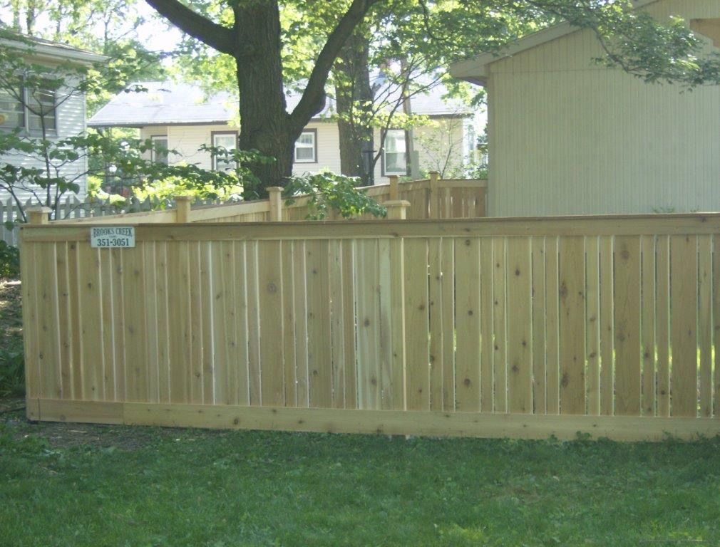 Wooden fence in a backyard, with a house and trees in the background.