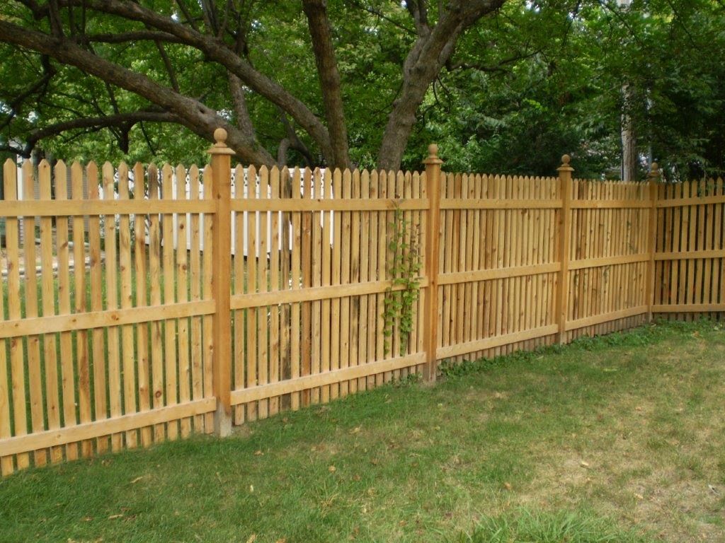 Wooden picket fence in a grassy yard, with trees in the background.