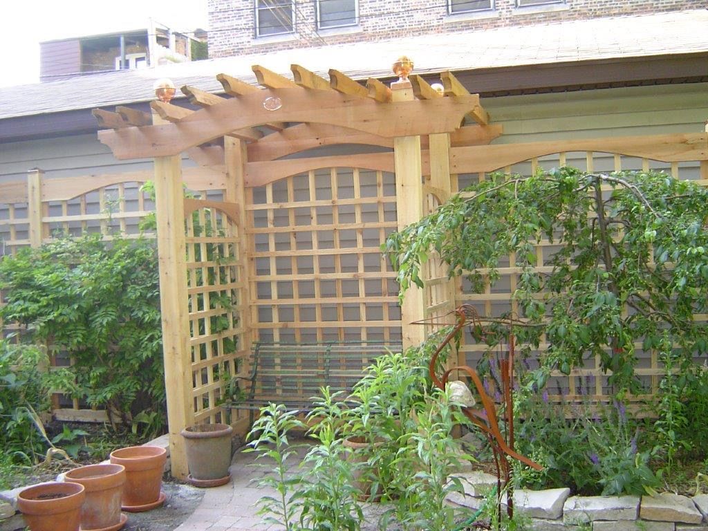 Wooden pergola entrance to a garden with lattice walls and lush green plants.