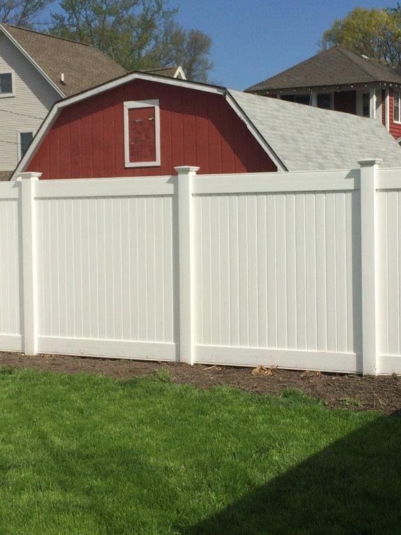 White vinyl fence in front of red barn with a white roof, under a blue sky.