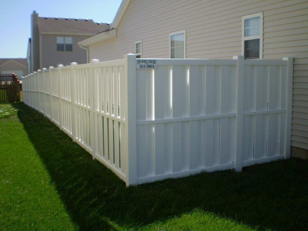 White vinyl privacy fence in a backyard, beside a beige house.