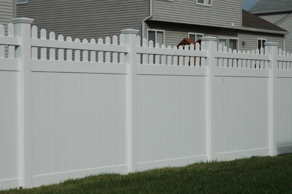 White vinyl fence with a picket top, enclosing a grassy yard; houses in the background.