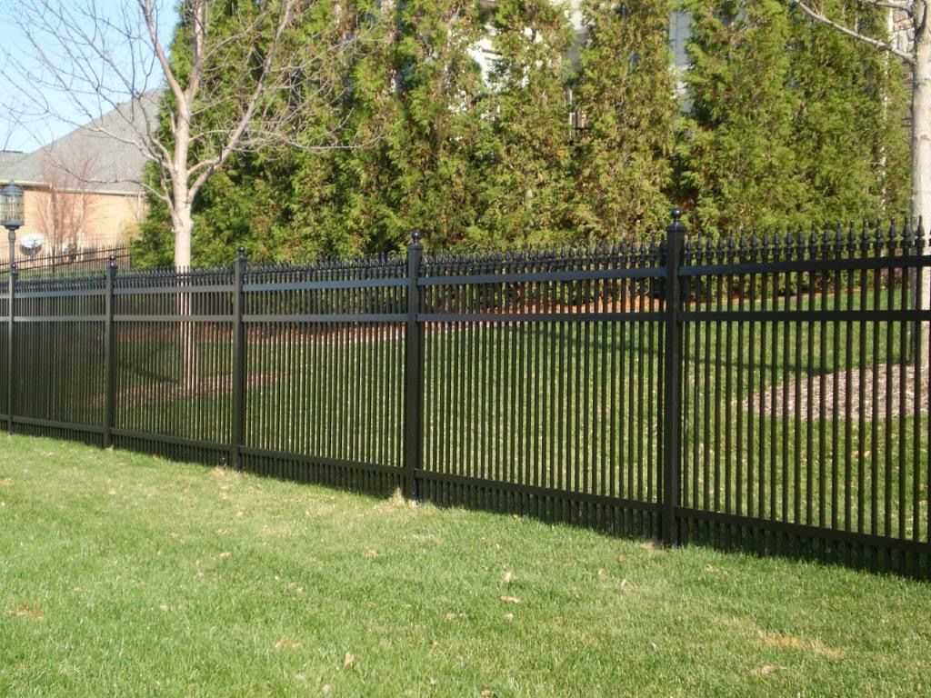 Black metal fence on green lawn, trees in background.