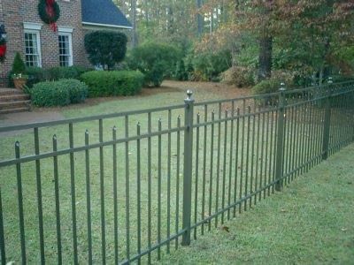 Black metal fence borders a green lawn in front of a house.