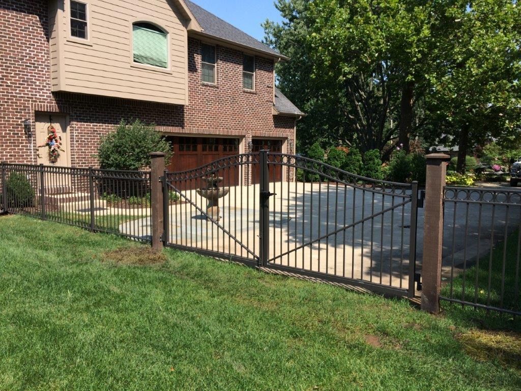 Black iron fence and gate in front of a brick house with a green lawn.