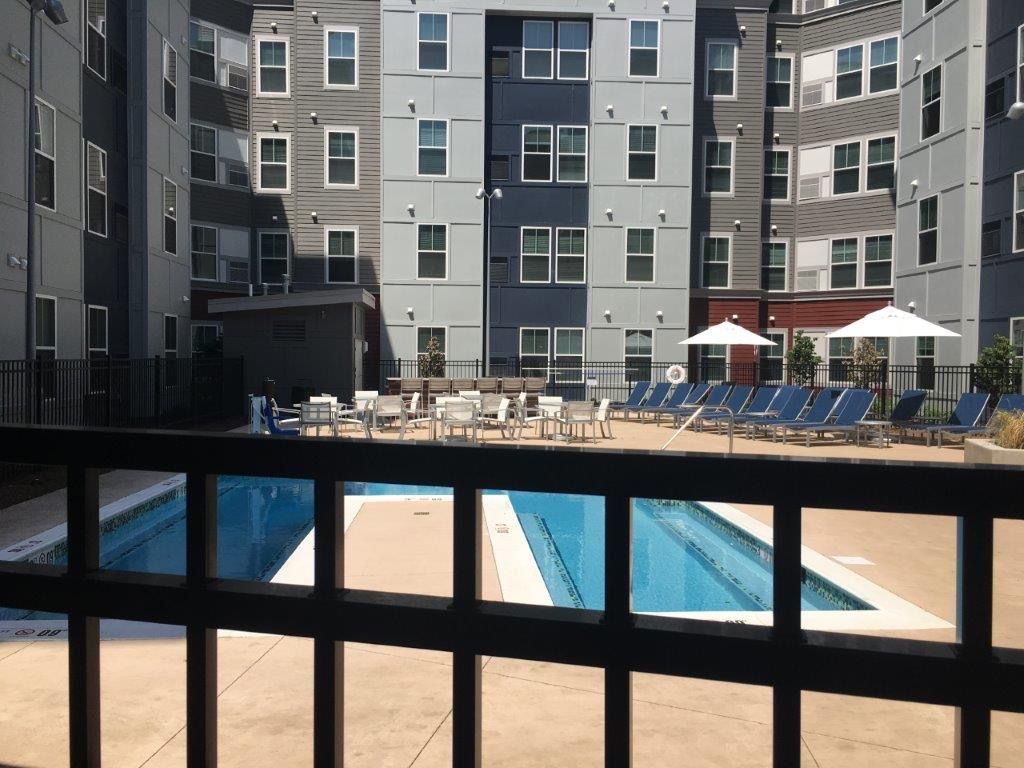 Pool and lounge chairs in courtyard of apartment building. Blue, gray, and white facade.