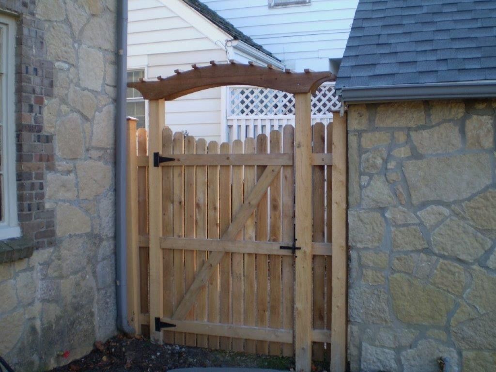 Wooden gate with an arched top, set between stone walls.
