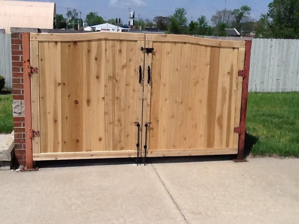 Wooden double gate with metal hardware, set between brick and metal posts, on a concrete surface.