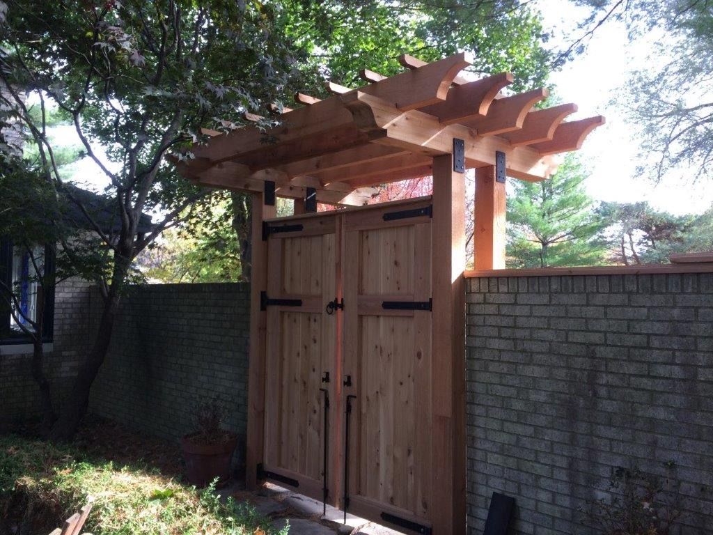 Wooden gate with pergola roof, brick wall, and lush greenery.