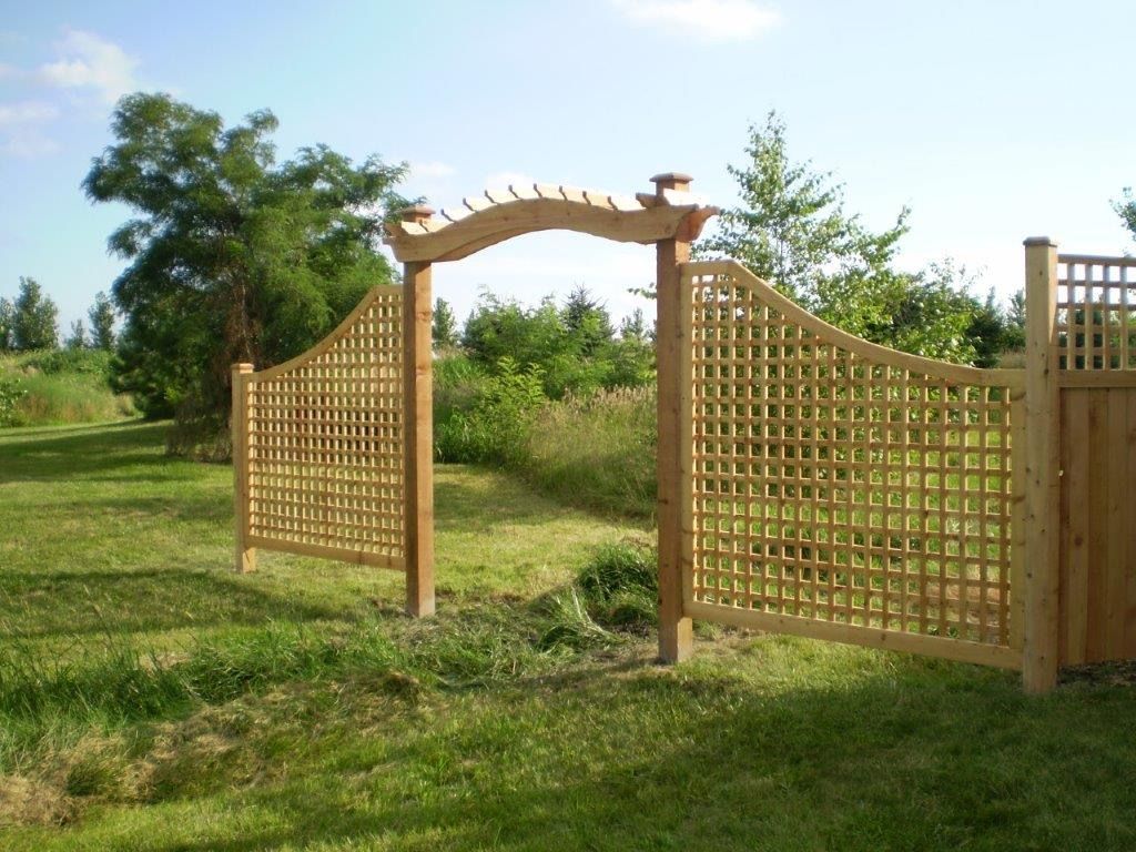 Wooden garden gate with latticework and arched arbor opening onto a grassy field.