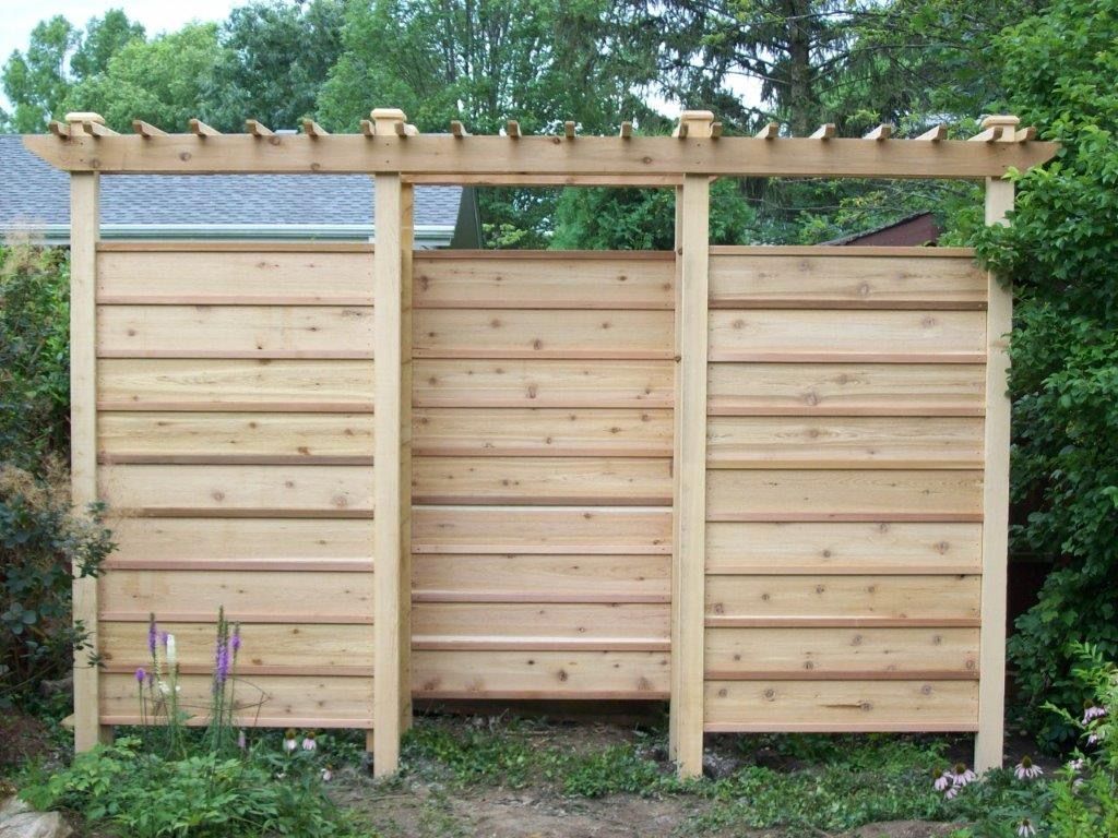 Wooden fence with horizontal planks and pergola top, in a garden setting.