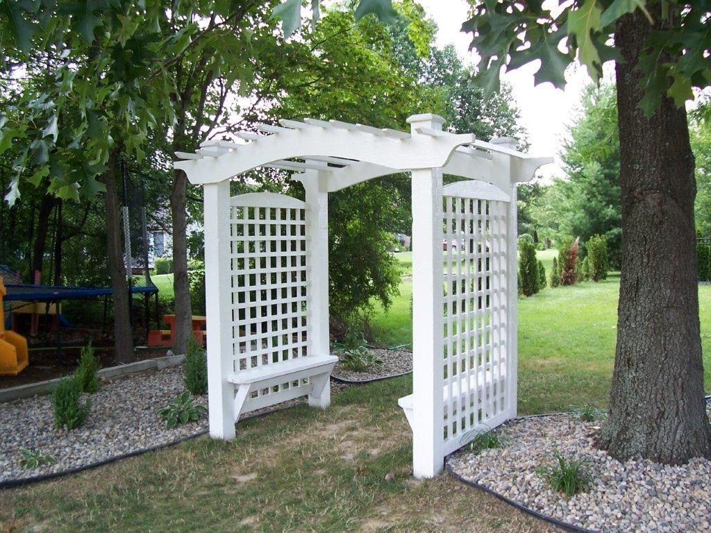 White wooden arbor with built-in benches, set in a backyard.