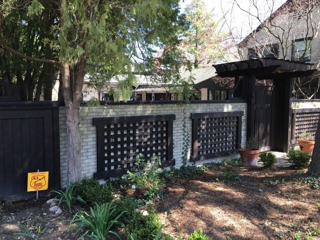 Black fence with lattice panels, brick and wooden gate, and a garden.