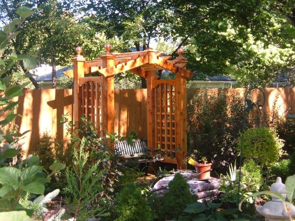 Wooden garden arbor with trellis sides and small garden bed.