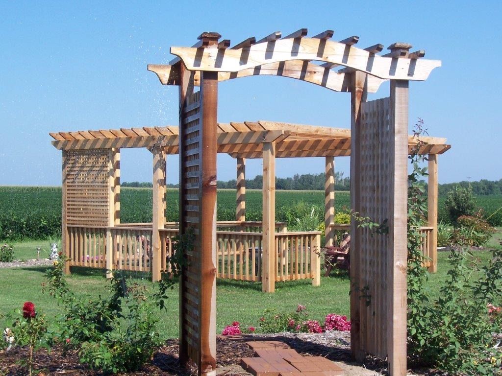 Wooden pergola and archway in a garden, with green grass and a blue sky.
