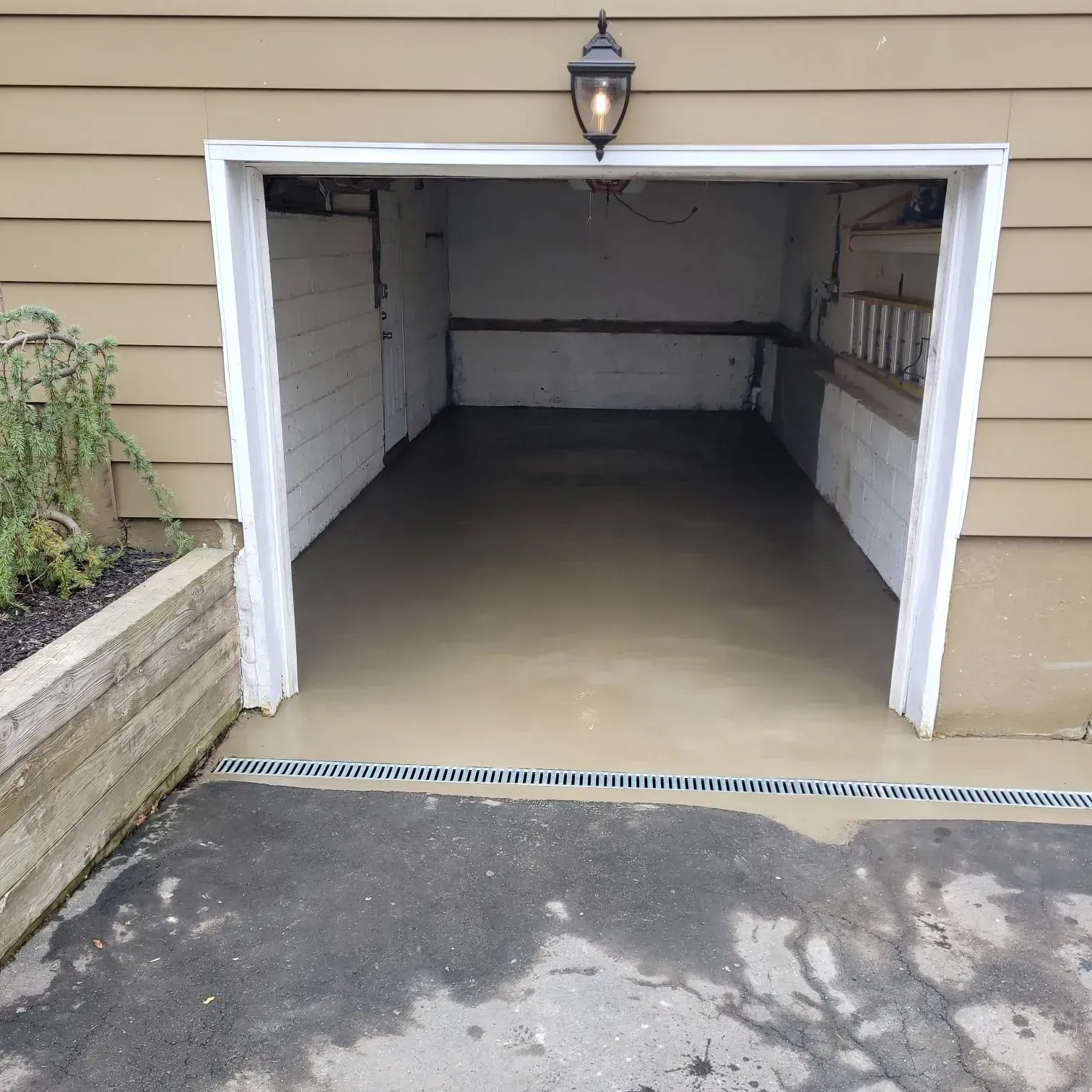 Garage with white trim, tan siding, and a light fixture, with a gray concrete floor and driveway.