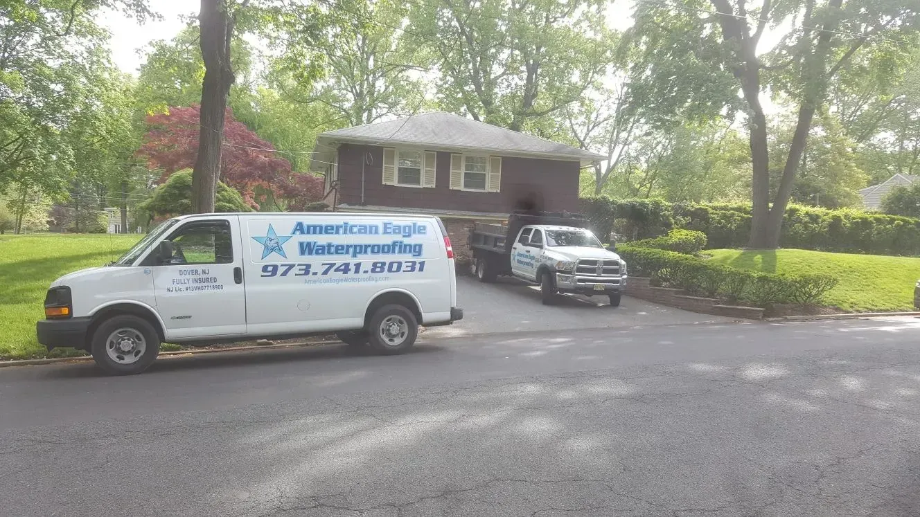 White van and truck with a trailer parked in front of a house, likely for waterproofing services.