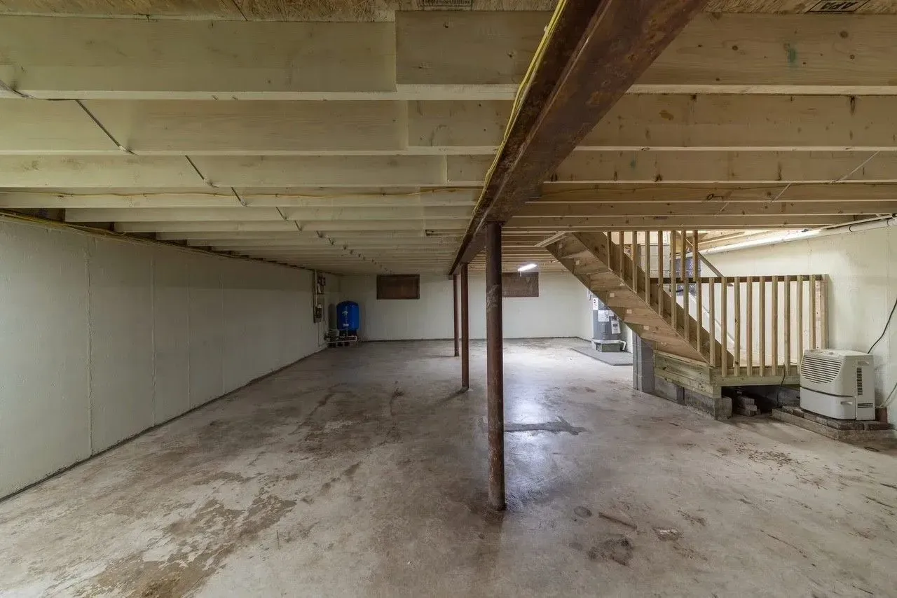 Basement with concrete floor, exposed wooden beams, support posts, and a staircase.