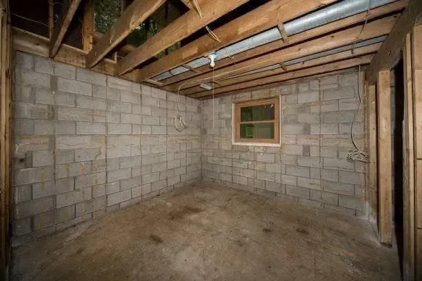 Basement room with concrete block walls, small window, wooden ceiling beams, and concrete floor.