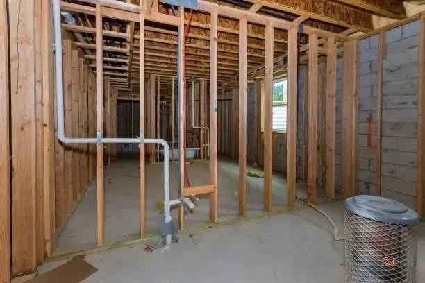 Framed basement with exposed wood studs, plumbing, and a small space heater.