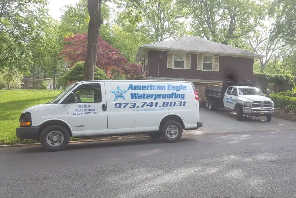 White van and truck with "American Eagle Waterproofing" parked in front of a house.