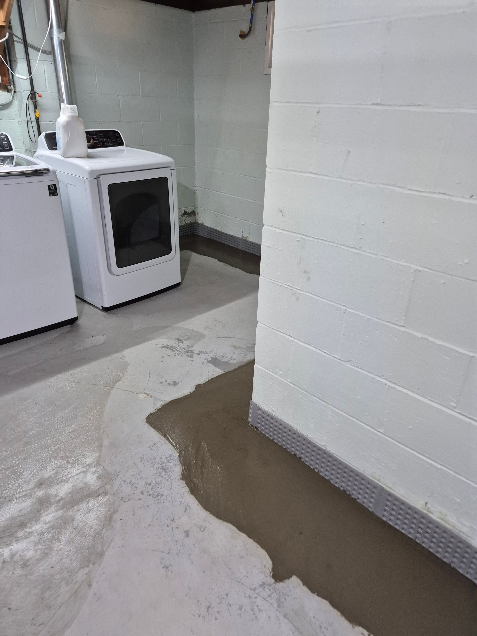 Basement with wet concrete floor, white block walls, and a washing machine and dryer.