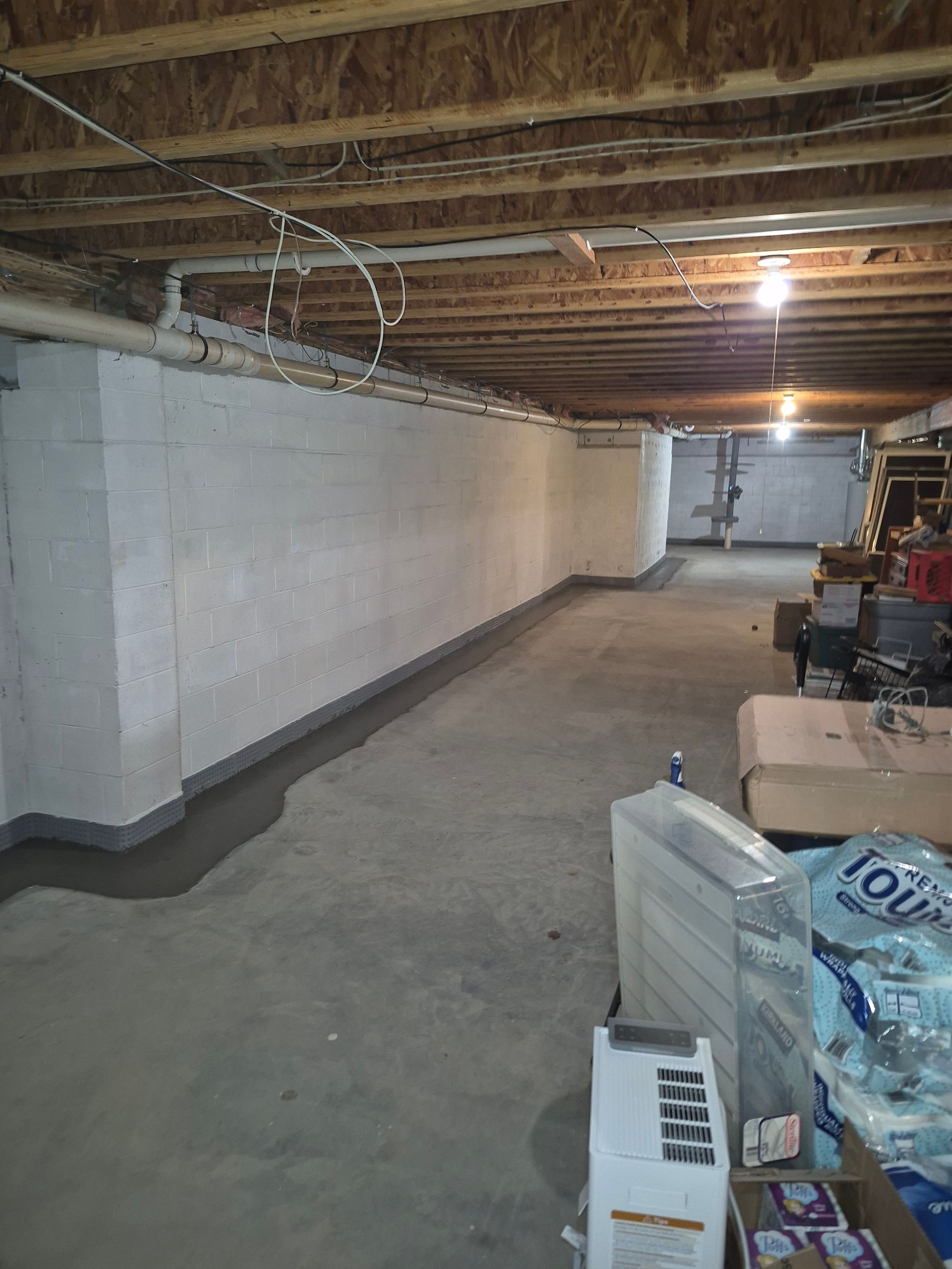 Basement with concrete walls and floor. A dark strip runs along the base of the wall. Debris is scattered on the floor.