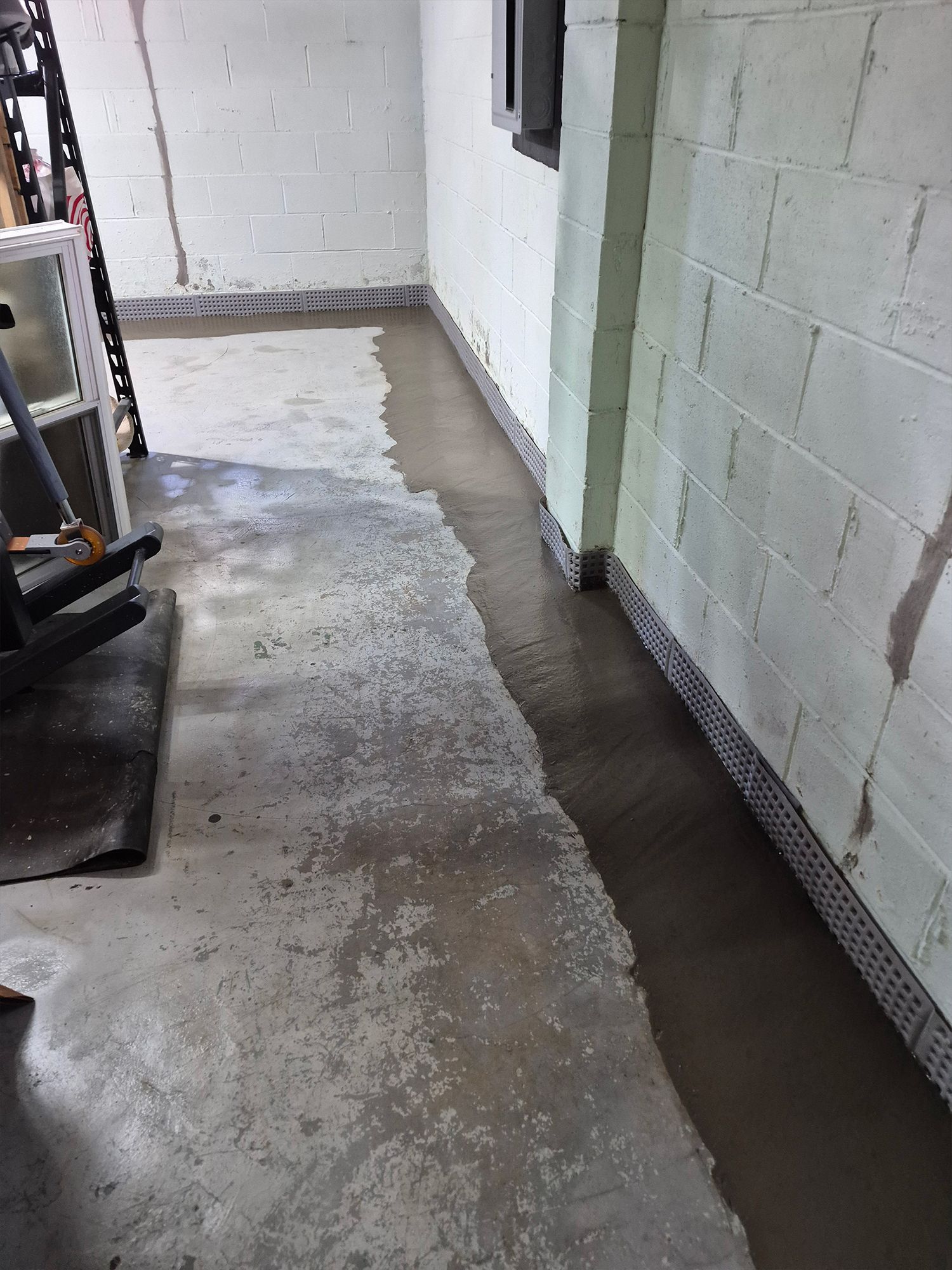 Concrete floor in a basement, with a strip of wet concrete along the walls.