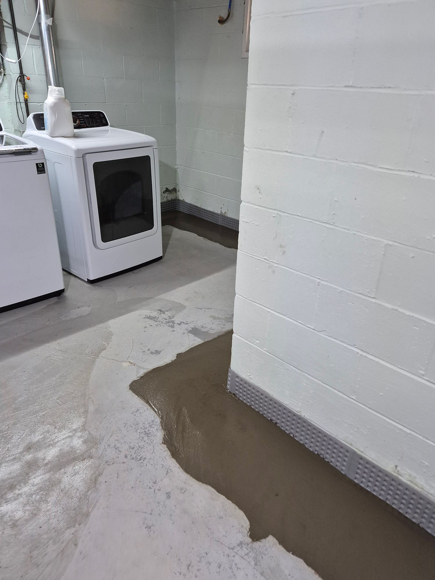 Flooded basement floor with water pooling near a white dryer and wall.