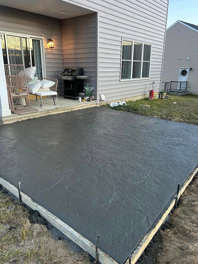 A freshly poured concrete patio next to a house with a door and windows.