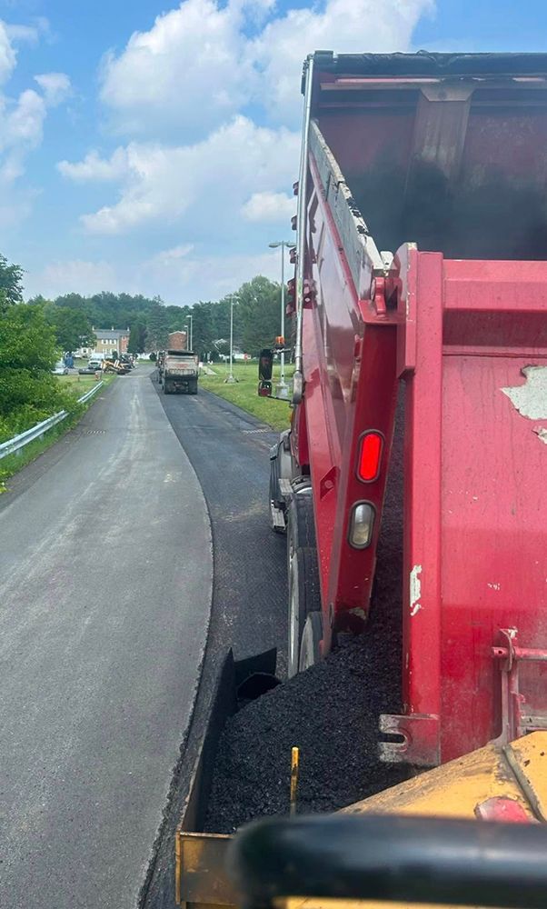 Red dump truck on a road; asphalt paving in progress.