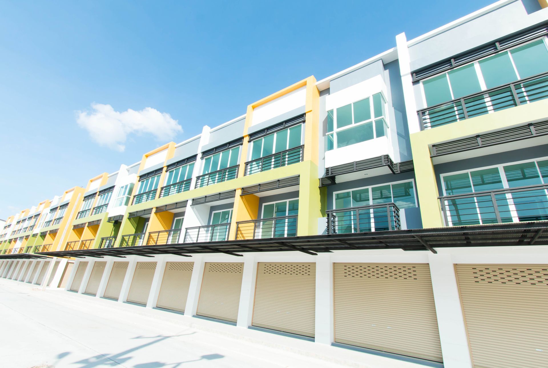 A low-angle view of a row of modern, multi-story townhouses with pastel-colored accents and rolling garage doors.