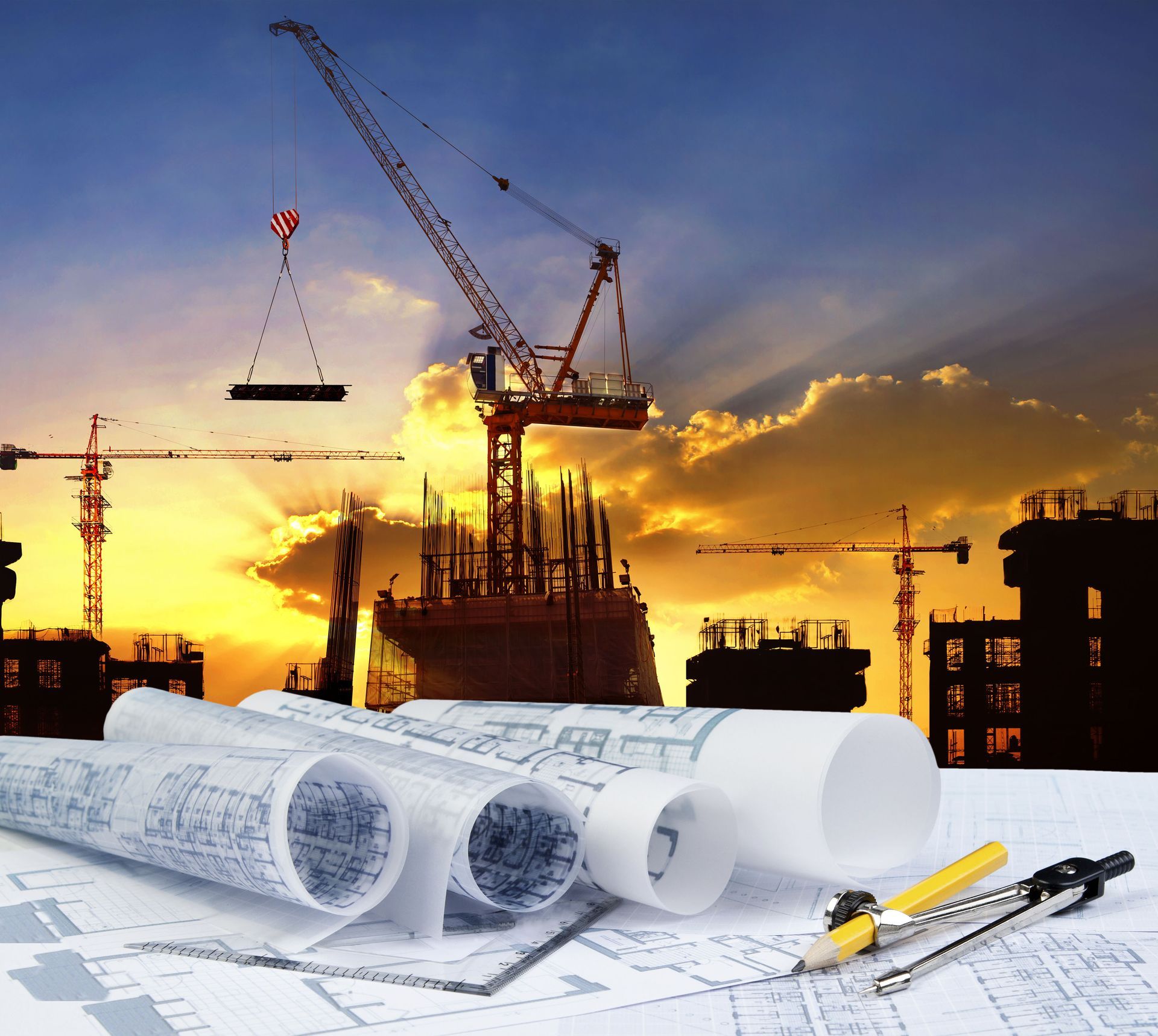 Construction site at sunset with blueprints and drafting tools in the foreground.