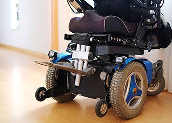Blue and black power wheelchair parked on a wooden floor in a hallway.