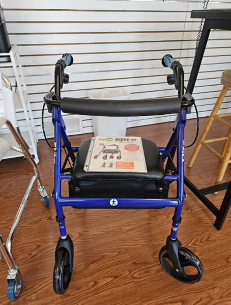 Blue rolling walker with seat, handles, and instruction sheet; indoors.