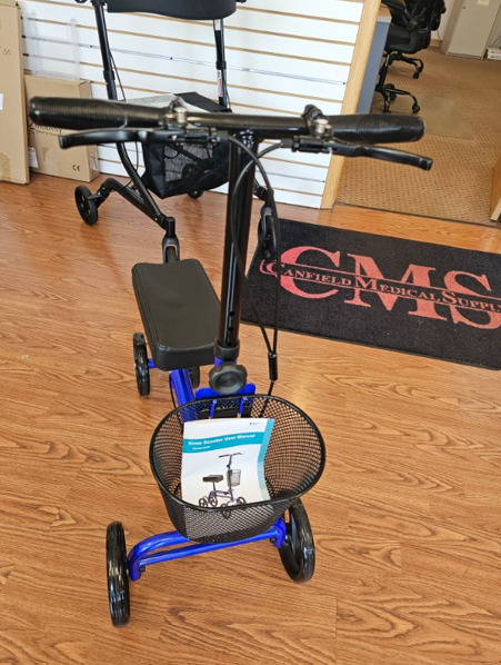 Blue and black knee scooter with basket and black handlebars, indoors next to a door mat.