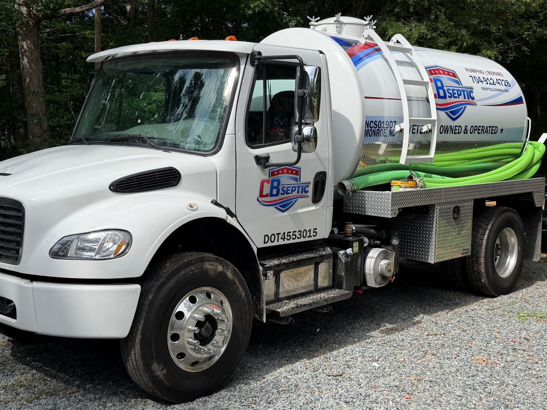 White vacuum truck with hose reels parked on gravel lot