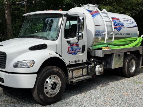 White vacuum truck with hose reels parked on gravel lot