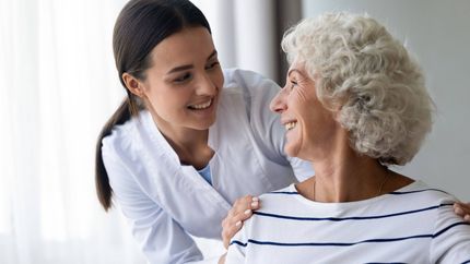 Two women smiling and talking closely in a bright, white room
