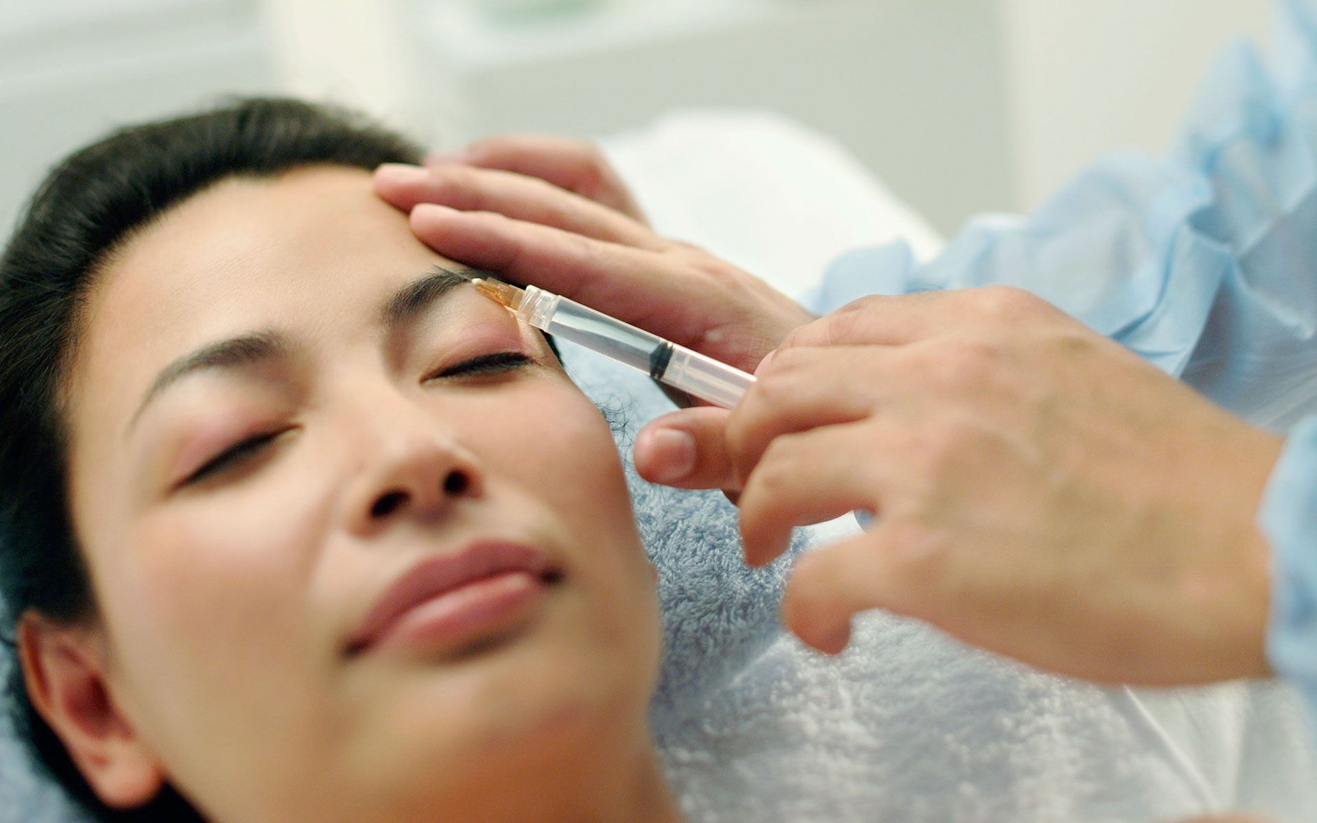 A woman is getting her eyebrows trimmed by a doctor