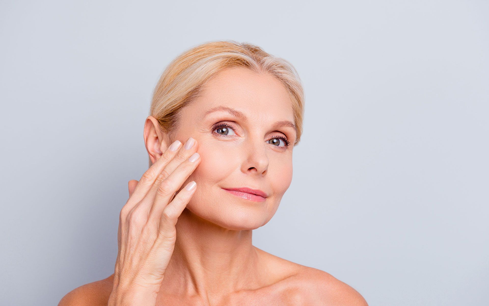 A woman is touching her face with her hand and smiling.