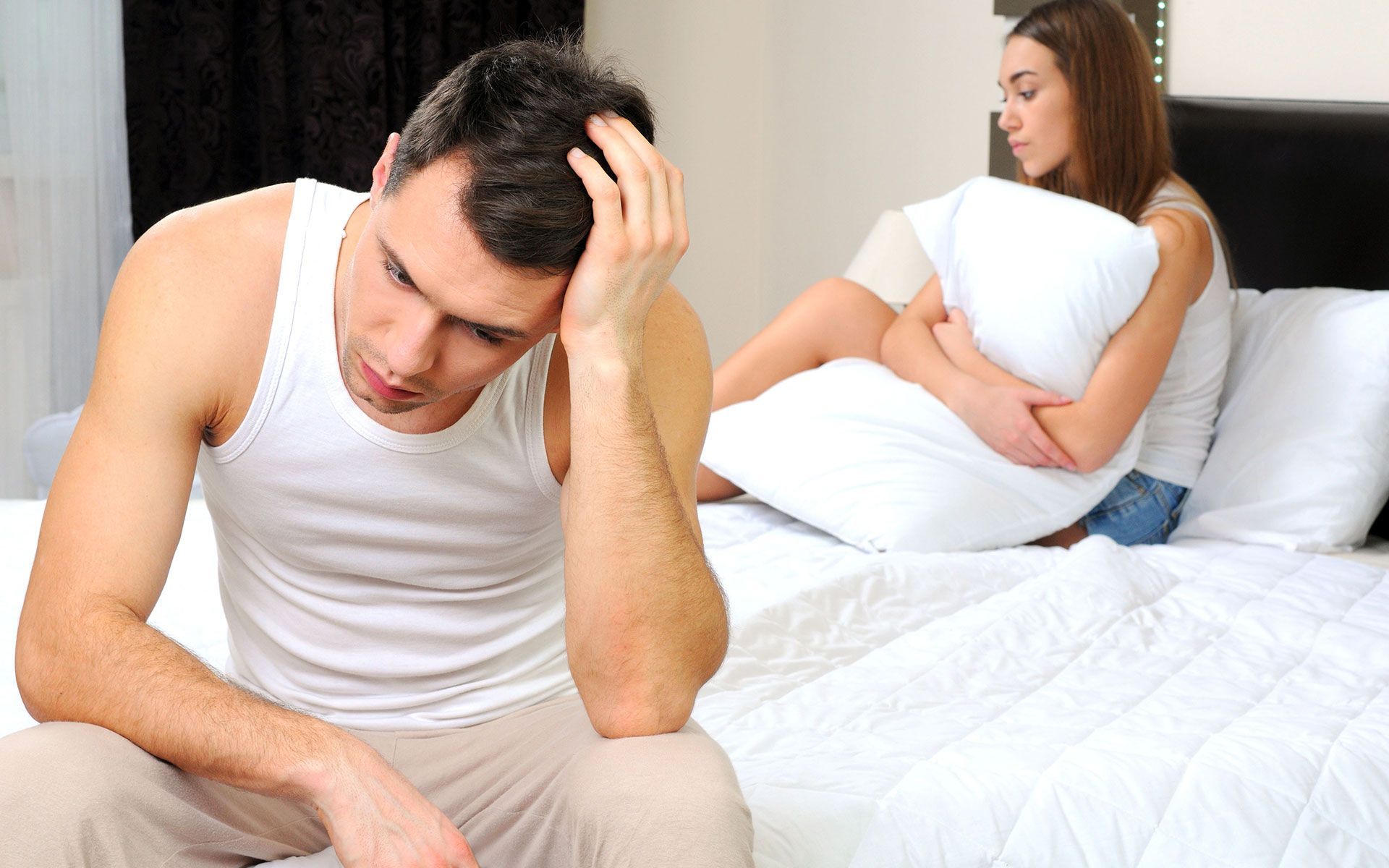 A man is sitting on a bed next to a woman holding a pillow.