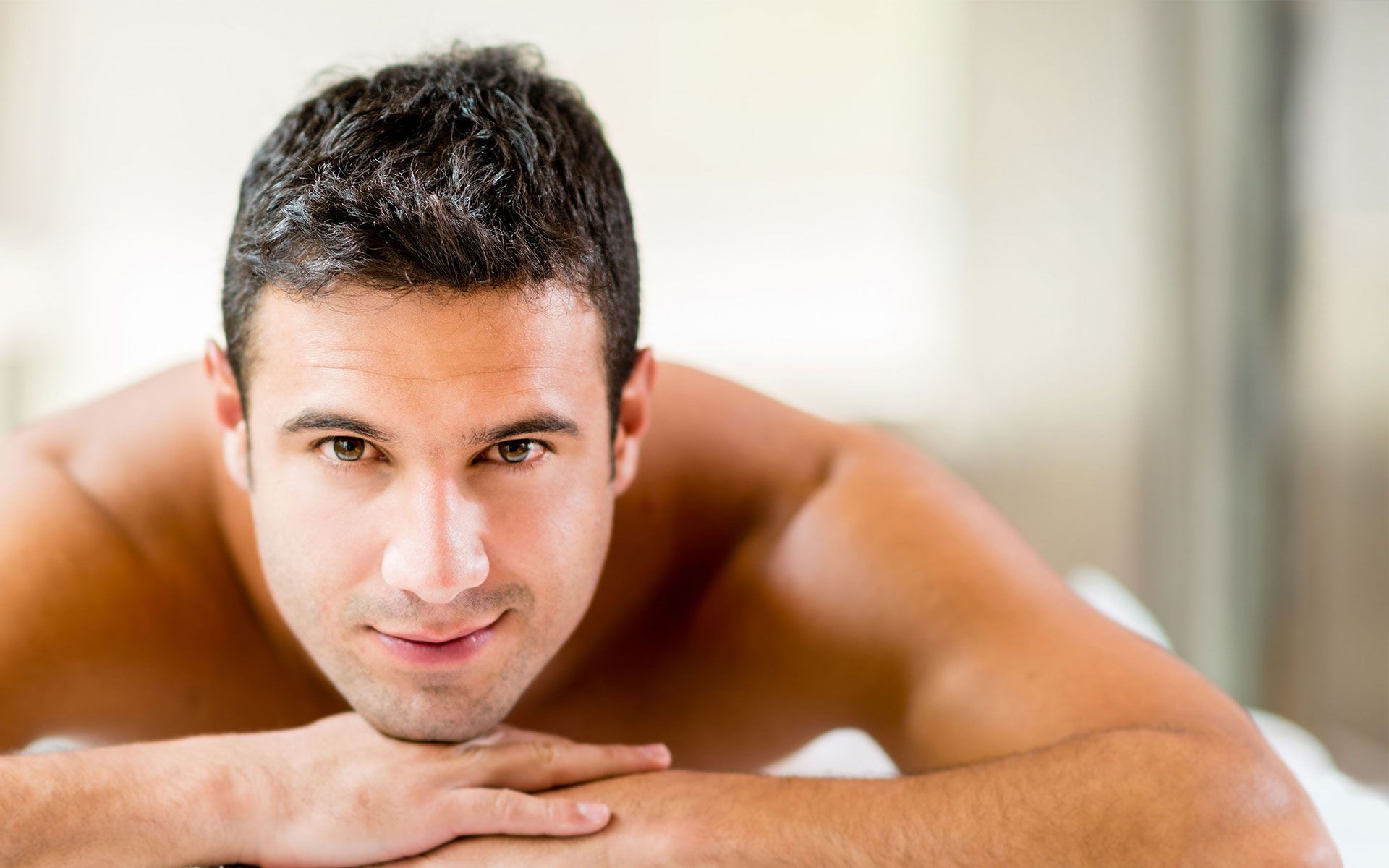 A shirtless man is laying on a massage table with his hands on his chin.