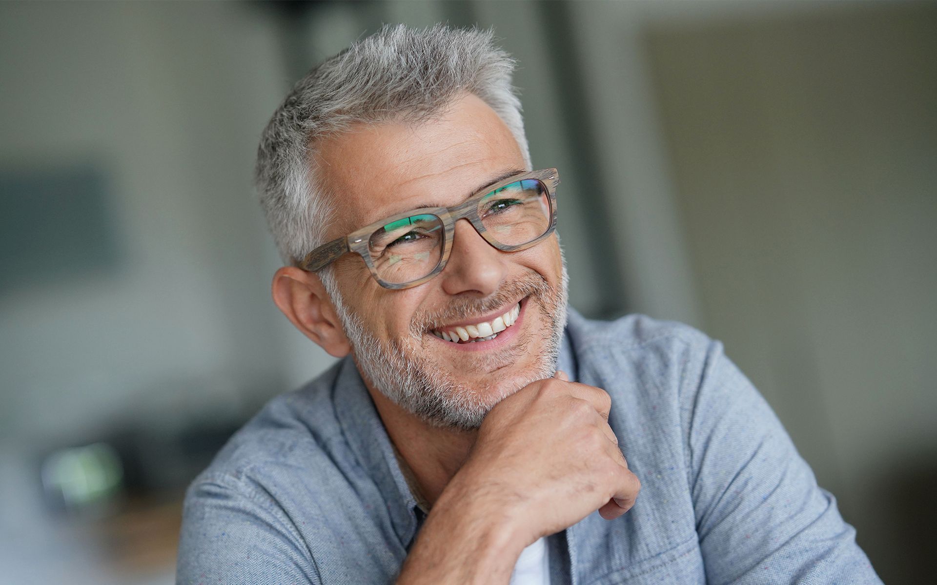A man with glasses and a beard is smiling with his hand on his chin.