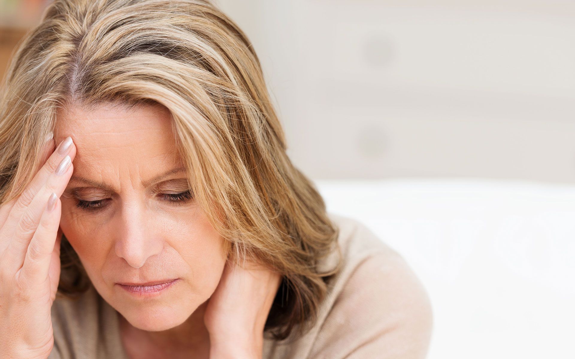 A woman is sitting on a couch with her hand on her forehead.