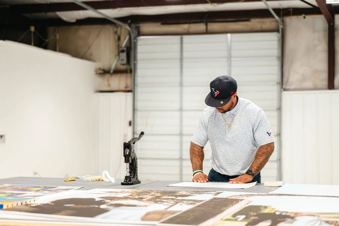 Person leaning over large prints on a table in a workshop, examining materials in a bright industrial space