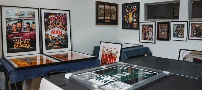 Framed comic posters and memorabilia displayed in a room with glass-top tables and black walls