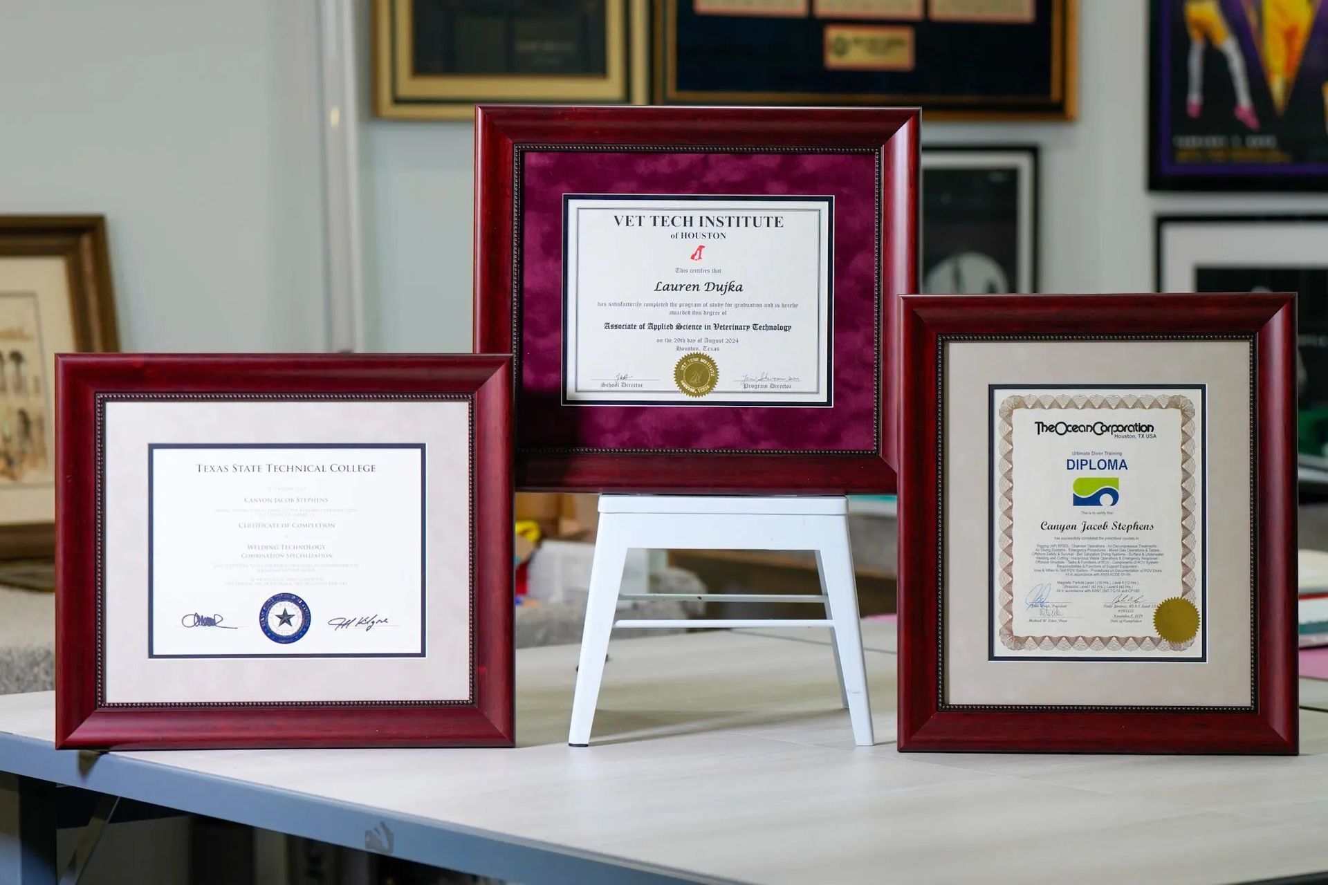 Three framed certificates displayed on a table, with a red frame in the center and two smaller frames on either side