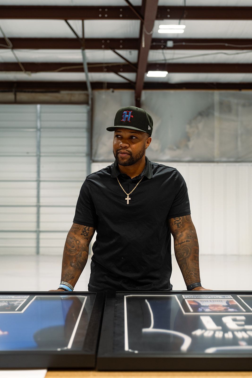 Man standing behind a table in a warehouse, wearing a black shirt and cap.