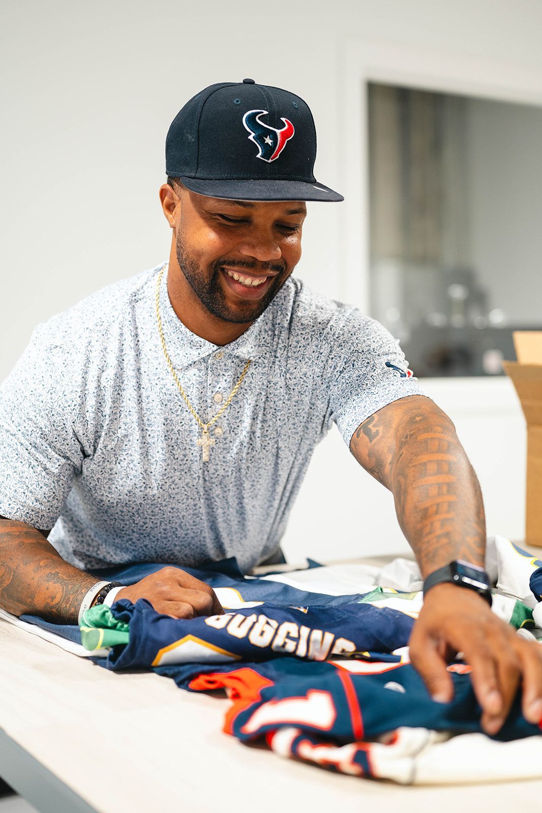 Man smiling while arranging sports jerseys on a table indoors